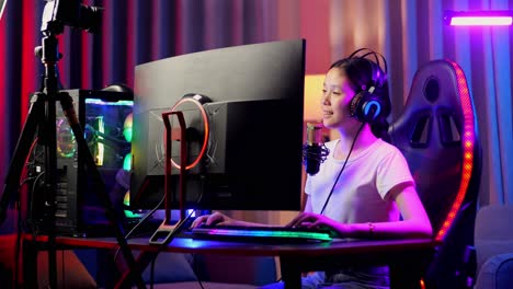 asian girl streamer playing game over network on personal computer, talking to the participants on the microphone.  live stream video game, desk illuminated by rgb led strip light