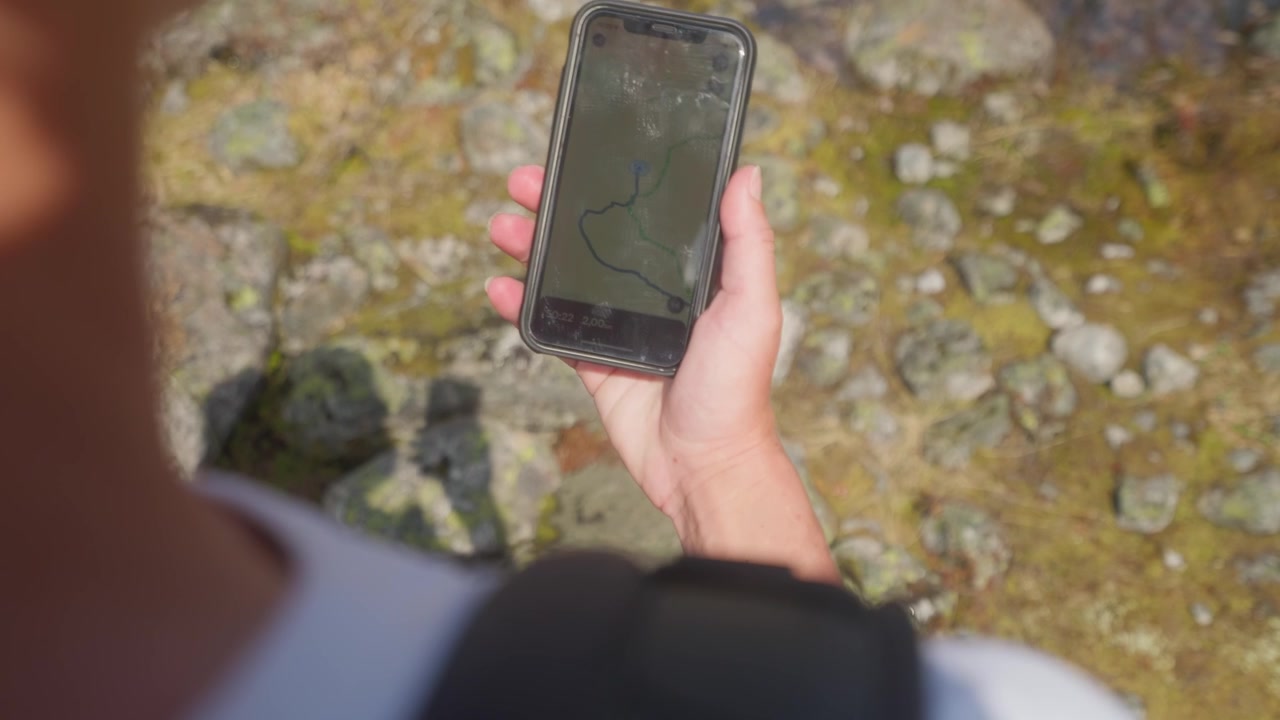 Ripresa POV da sopra la spalla di una mano che tiene uno smartphone con indicazioni di navigazione sullo schermo, ideale per concetti di escursionismo, ricerca di percorsi, viaggi ed esplorazione all'aperto