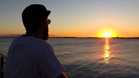 bearded man with rounded sun glasses staring at the sunset on a deck