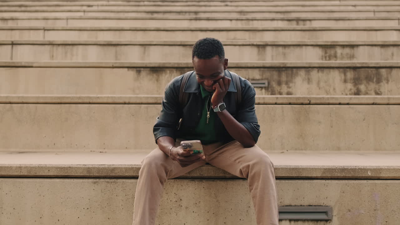Young African American Man Smiling While Using Smartphone on Concrete Steps