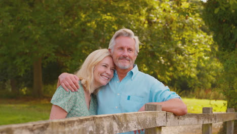 Sonriente-Pareja-Madura-O-Senior-Vestida-Informalmente-Apoyada-En-La-Valla-En-Un-Paseo-Por-El-Campo