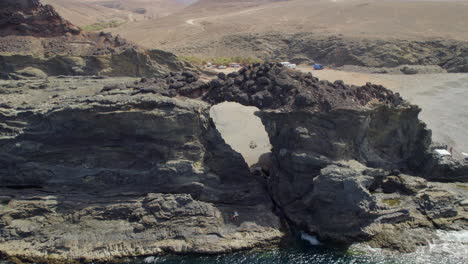 Fuerteventura-Island,-Ajui:-aerial-view-from-the-sea-traveling-in-over-the-Jurado-arch-on-a-sunny-day-with-beautiful-colors-and-turquoise-ocean