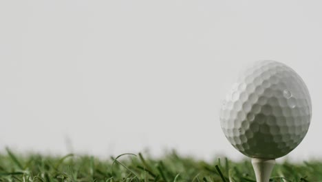close up of golf tee and ball on grass and white background, copy space, slow motion