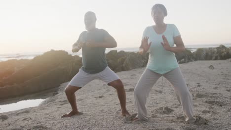 Feliz-Pareja-Afroamericana-Mayor-Haciendo-Yoga,-Estirándose-En-La-Playa,-Cámara-Lenta