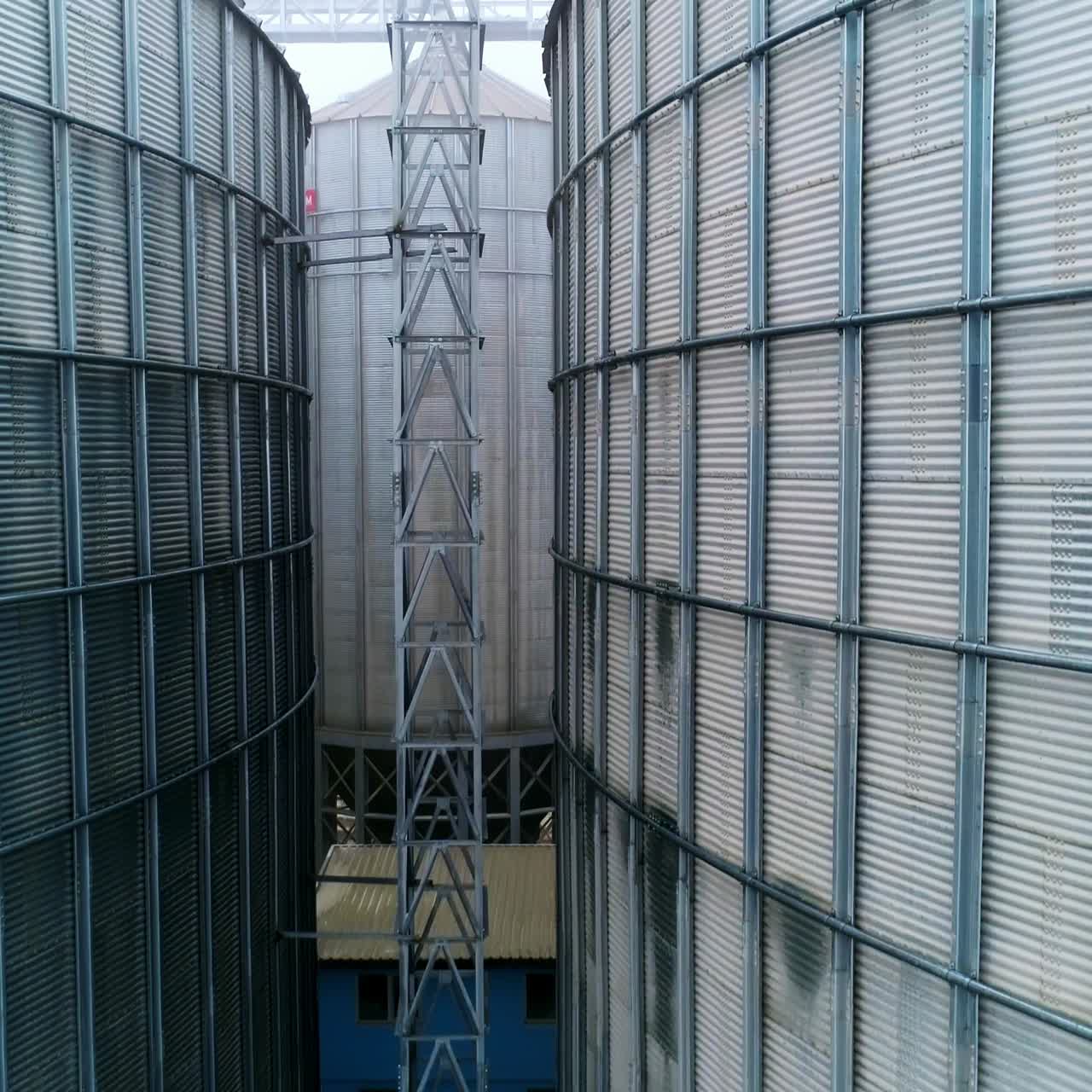 Going up between two metal elevator tanks to the tops. Exterior of steel granary bins on grey misty day