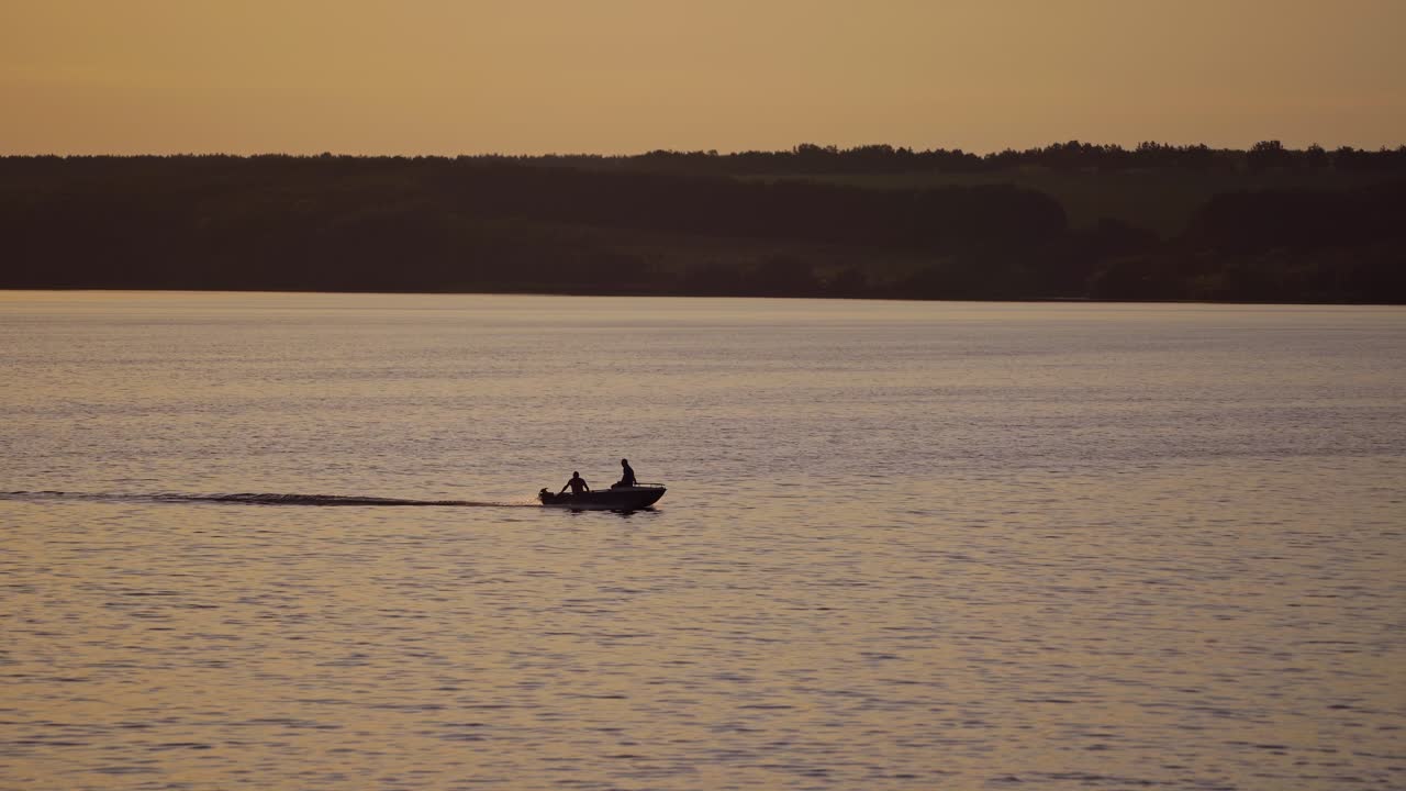 Motor boat floating in water on the forest background at dusk. Two people in a boat swimming along the river in the evening.
