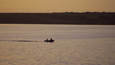 motor boat floating in water on the forest background at dusk. two people in a boat swimming along the river in the evening.