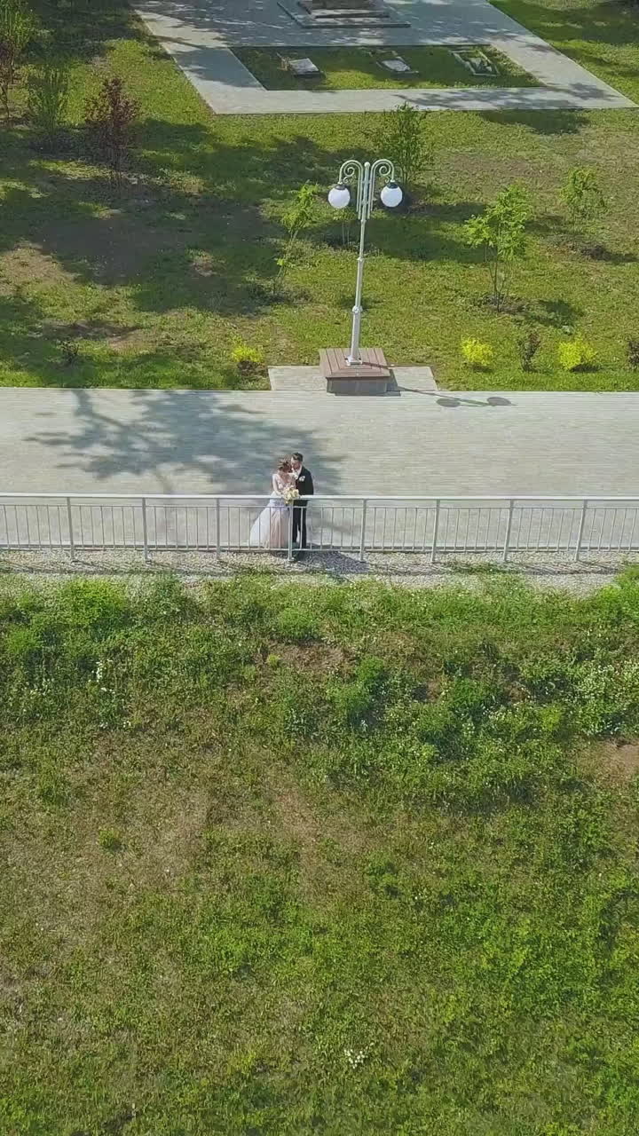 distant newlywed couple near handrail on road in beautiful green park on sunny autumn day aerial view