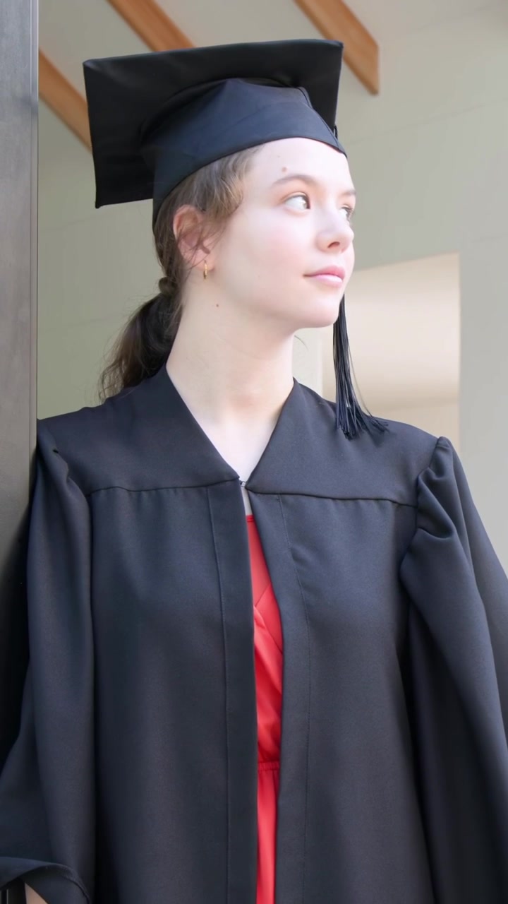 Vertical video: After pose, gowned grad scanning living room, pivoting out for portrait with cap
