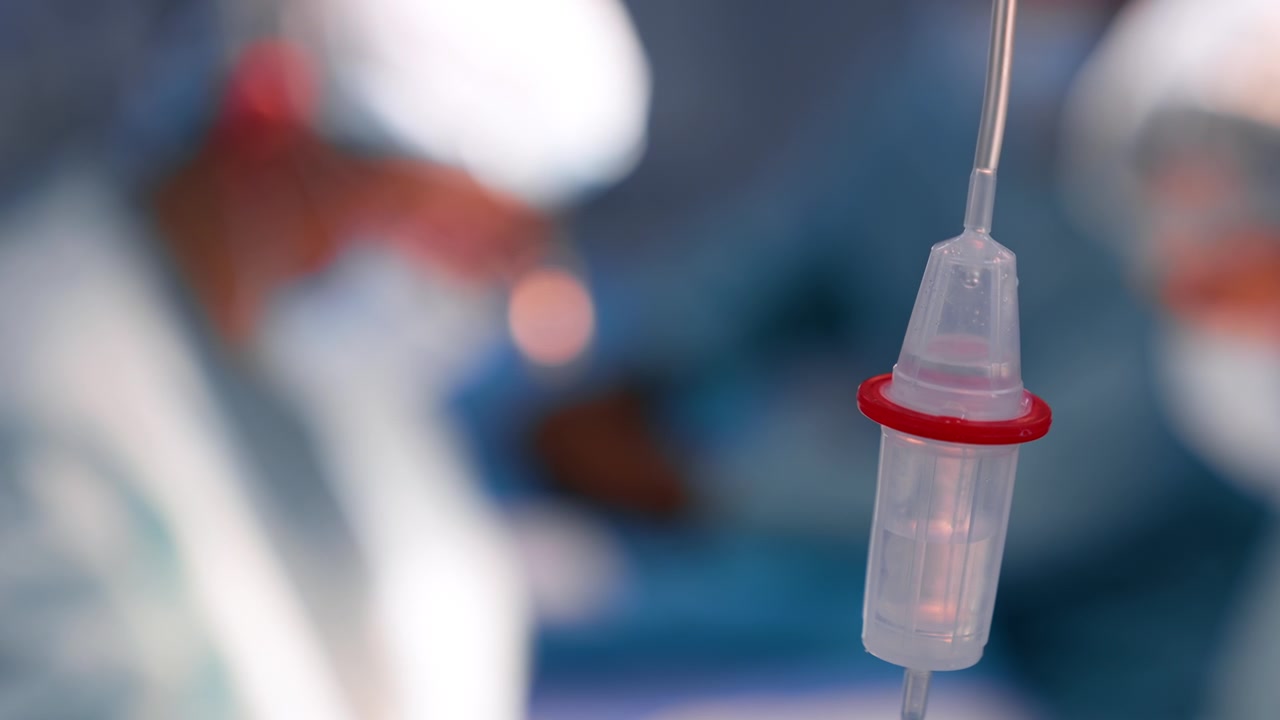 La soluzione gocciola all'interno del serbatoio del contagocce. Primo piano. Sagome sfocate di medici sullo sfondo.
