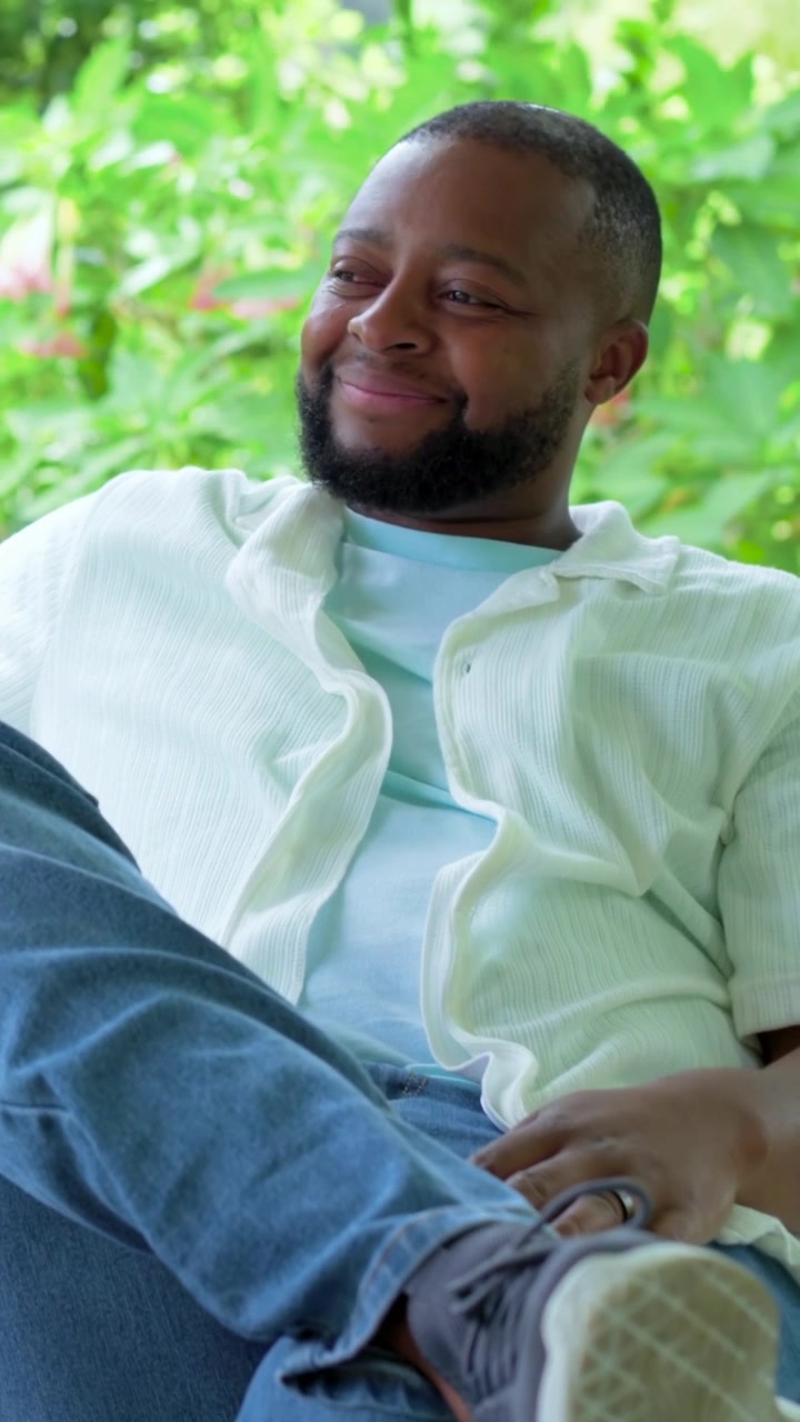 Vertical video: Reacting to offscreen cue, man smiling and shifting gaze on porch chair, copy space