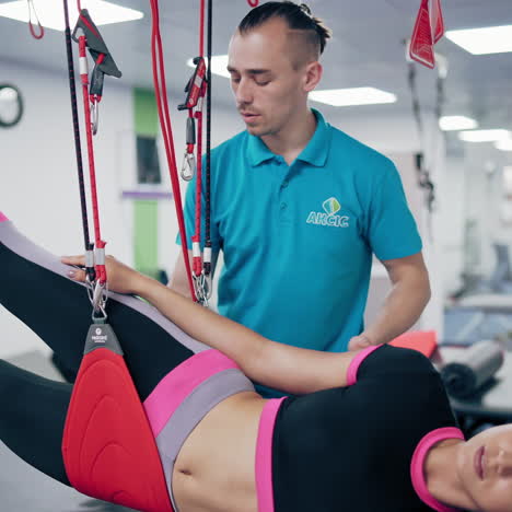 attractive young woman is doing exercises with suspension ropes in rehabilitation center. therapist instructor supports his patient at workout to recover after the injury.
