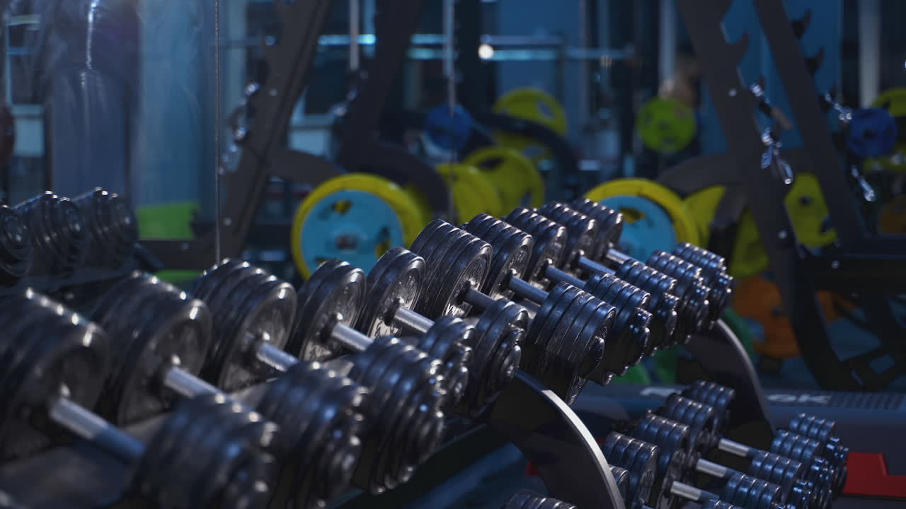 Set of modern sports equipment in the gym. Lifting dumbbells for bigger biceps. Muscular man coming to the dumbbells.