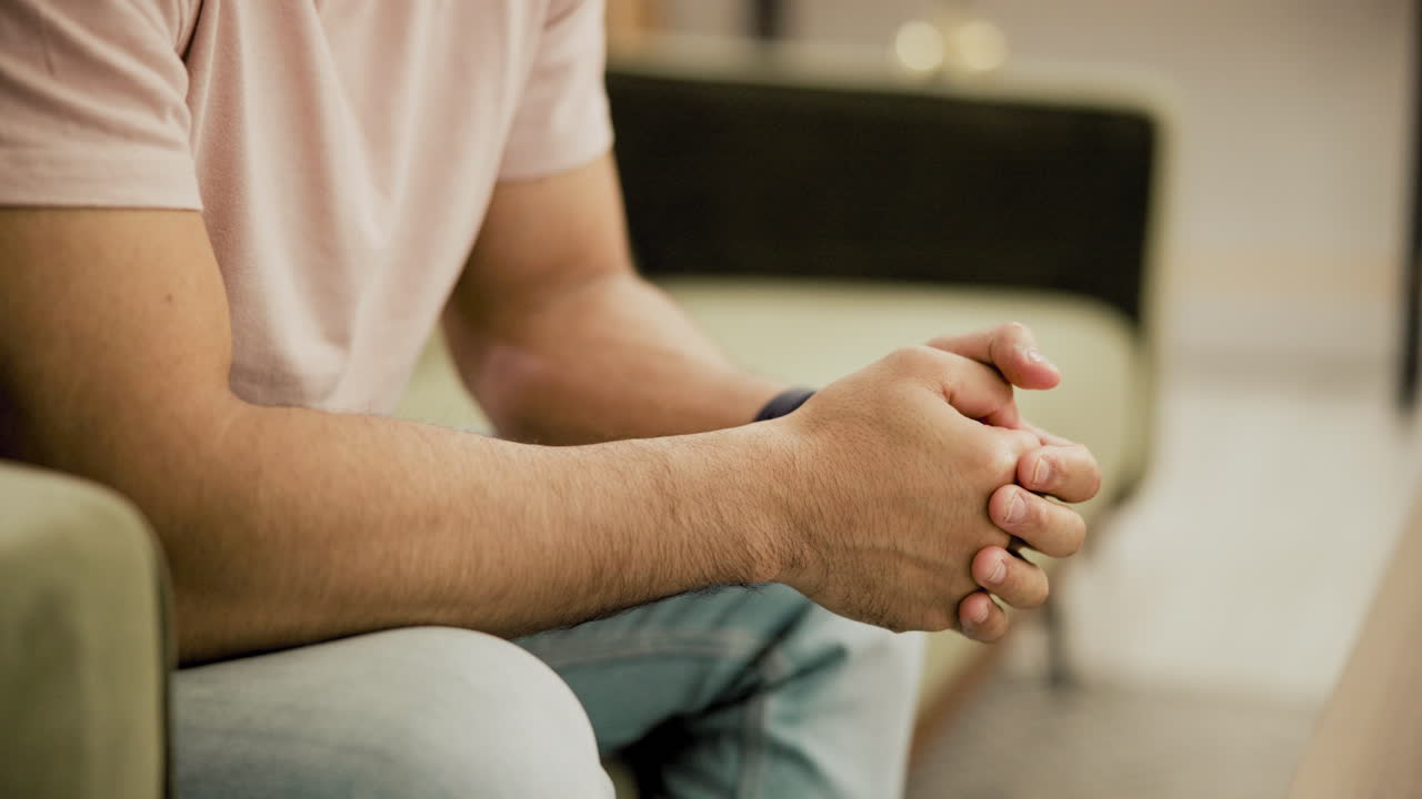 Homme assis sur un canapé, les mains jointes, en pleine conversation détendue