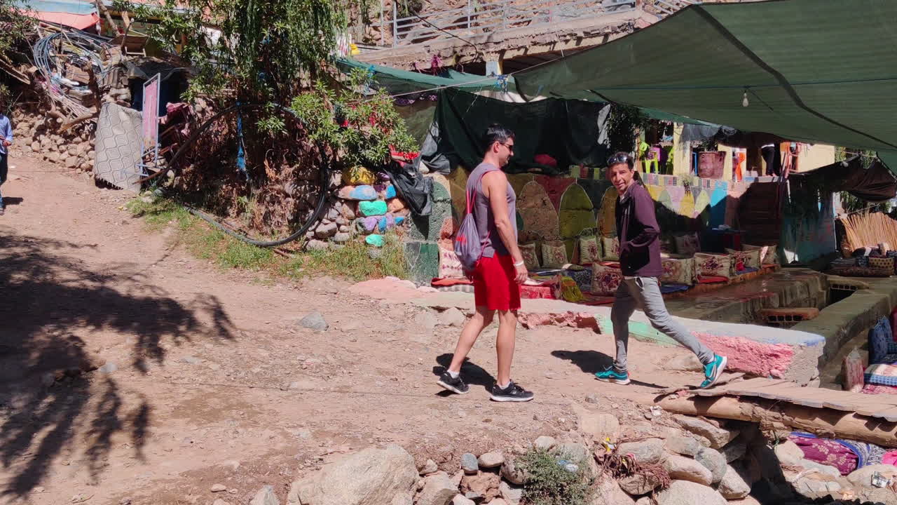 Man walking through colorful market in Ourika Valley, Morocco under shaded canopy