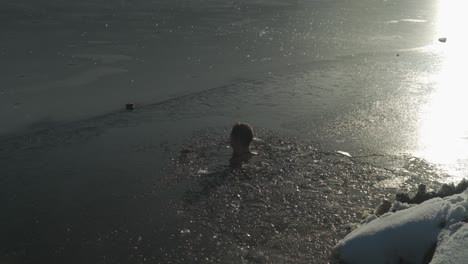 Young-man-sitting-neck-deep-in-freezing-cold-water-of-mountain-lake-after-breaking-ice-to-enter-frigid-environment