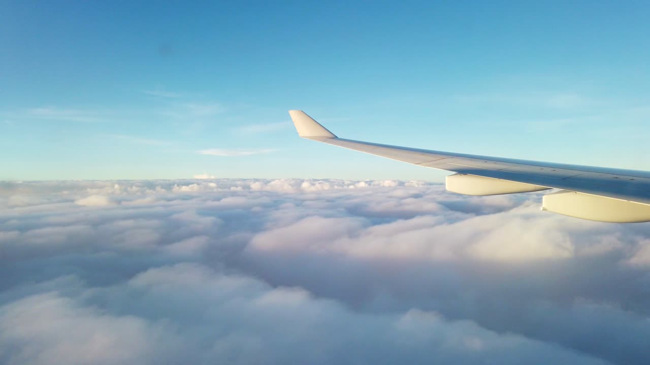 View from the airplane's left window during late afternoon, gliding above clouds a few hundred meters high