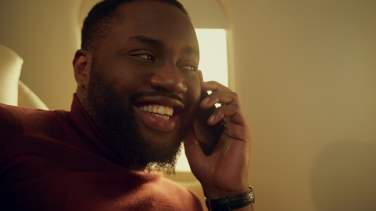 African american talking cellphone at airplane window closeup. First class guy