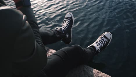 person sitting by water with converse shoes