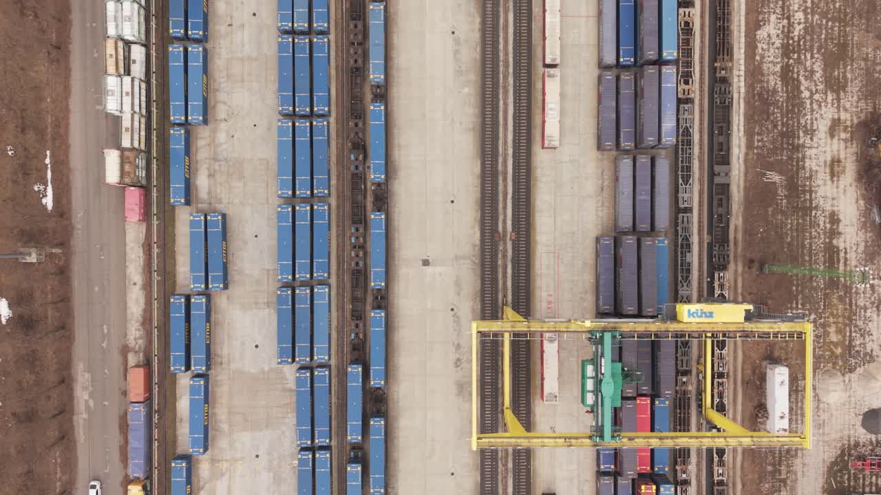 Luftfoto fra oven af en stor industriel fragtterminal med rækker af blå fragtcontainere og parallelle jernbanespor.