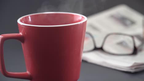 taza de café de la mañana con periódico y gafas de lectura en el fondo