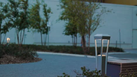 Urban-design-pedestrian-bollard-street-light-illuminated-at-dusk-in-a-city-park-setting