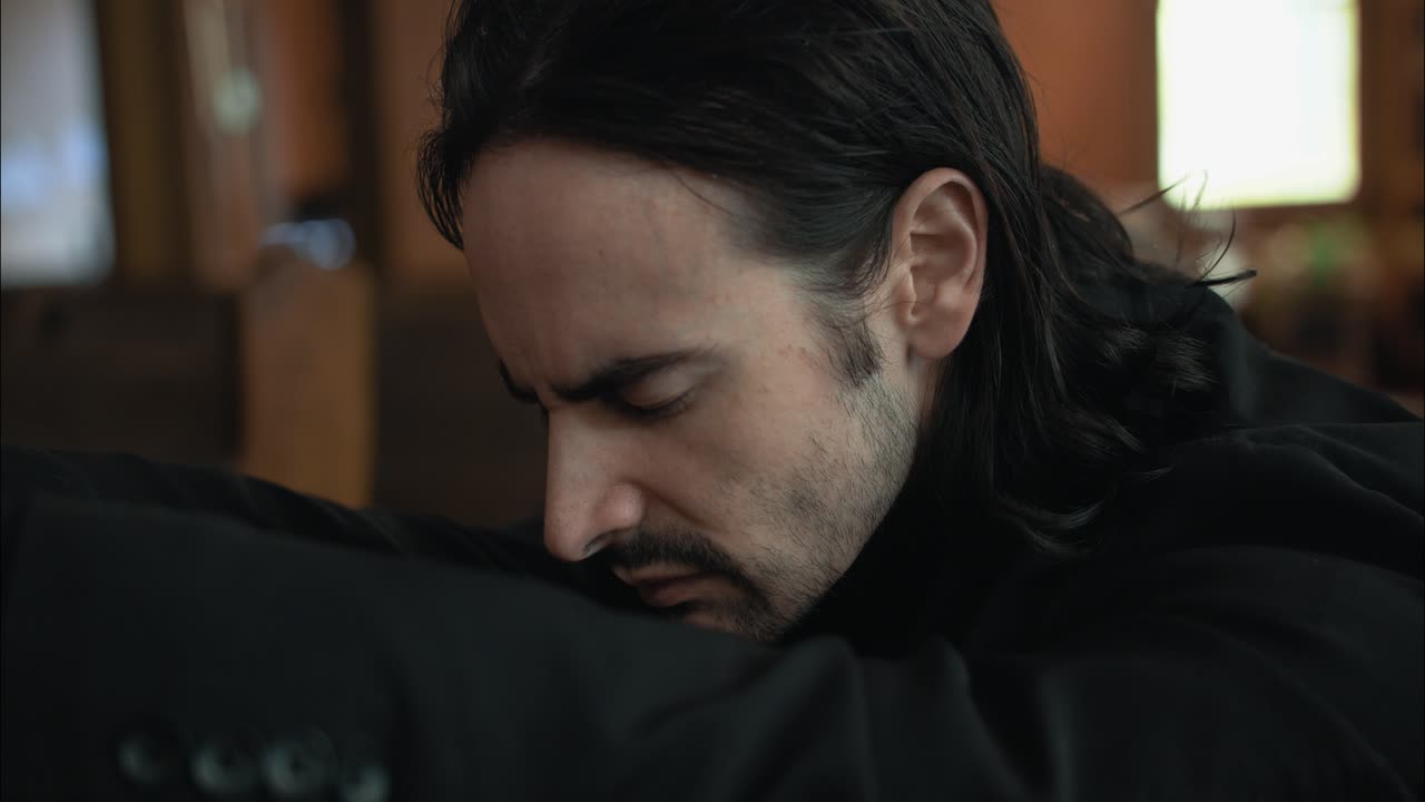 Jovem de terno preto orando no banco da igreja em câmera lenta cinematográfica com as mãos postas.