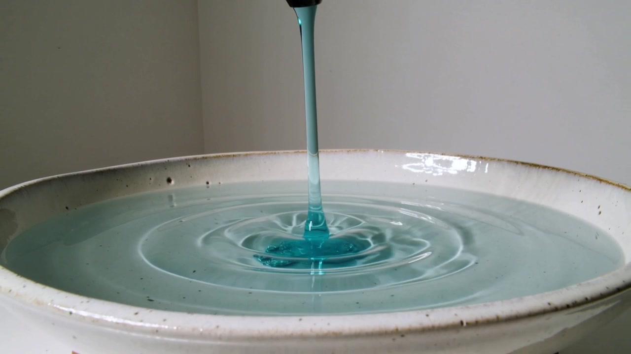 Spout pouring viscous turquoise liquid forming center mound and ripples in bowl on tabletop
