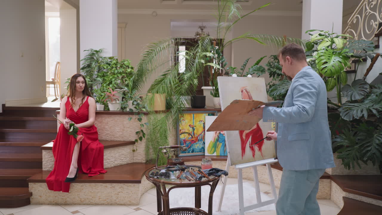 el artista dibuja el retrato de la hija en el estudio. la joven reina del baile de graduación en vestido rojo posa para el pintor sentado en el estudio de arte. creando la imagen de una modelo bonita