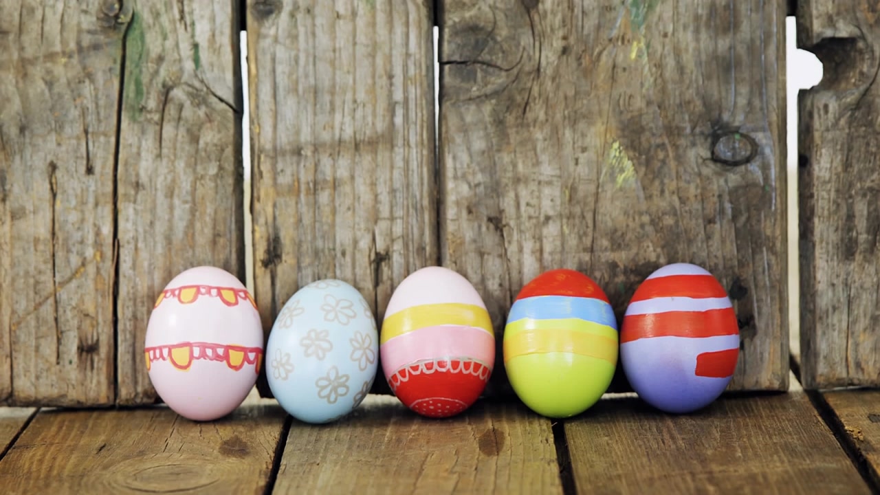 Descending five decorated eggs forming line on rustic tabletop, green overlay showing HAPPY EASTER