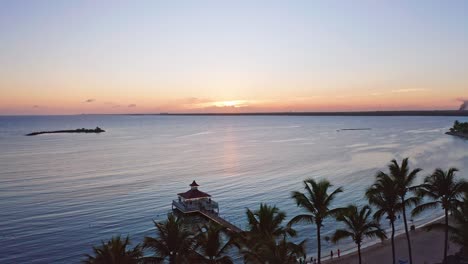 vista aérea que muestra el mar caribe tranquilo y la silueta de las palmeras en la playa y el puente peatonal durante la puesta de sol