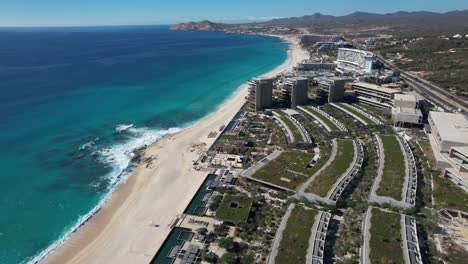 Mirando-Hacia-Abajo-En-El-Moderno-Complejo-Frente-Al-Mar-En-Los-Cabos-México-Con-Techos-De-Pasto--Panorámica-Aérea-Izquierda