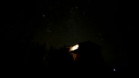 timelapse of dark starry sky moving, forest and cabin in foreground