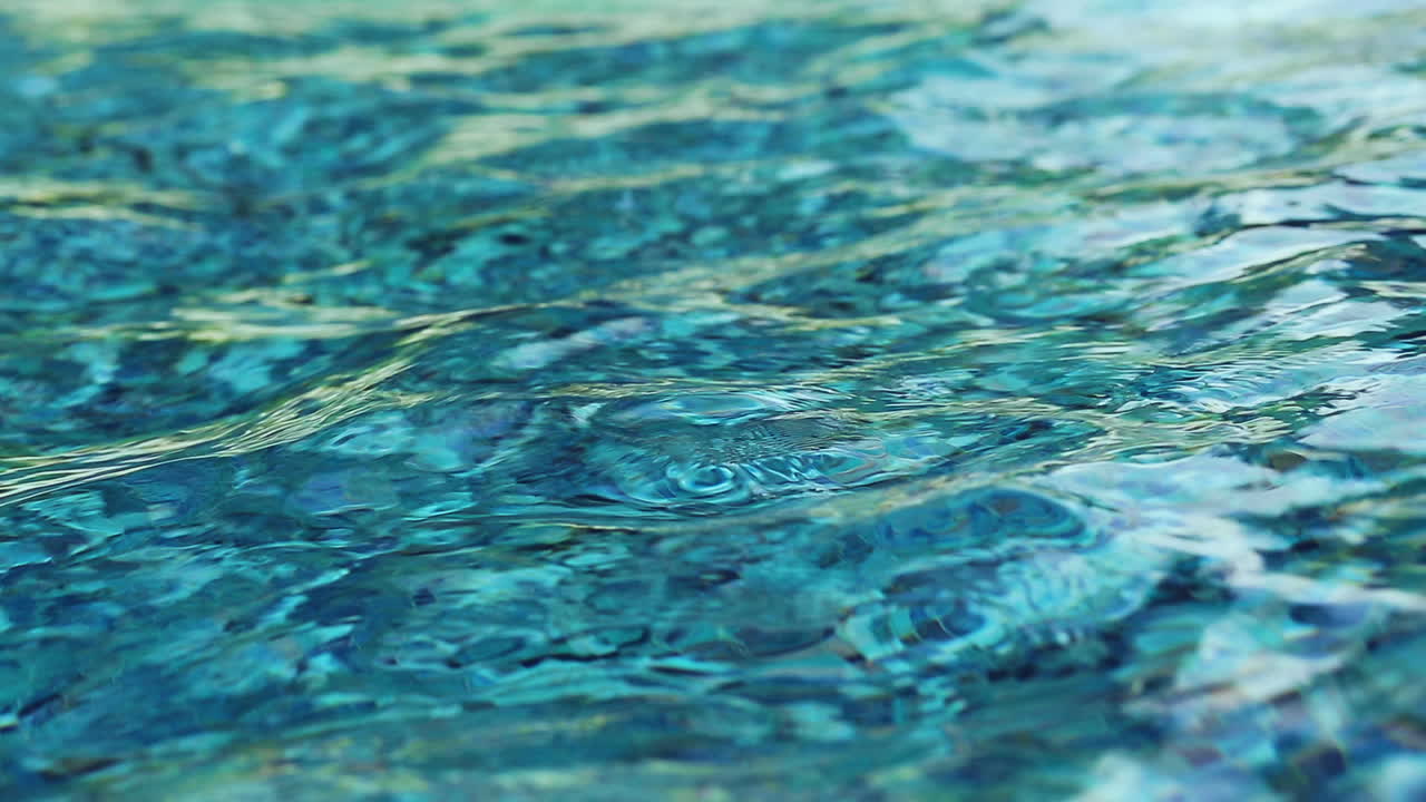 Above blue and teal mosaic tiles. Water ripples at the base of a fountains wishing well.