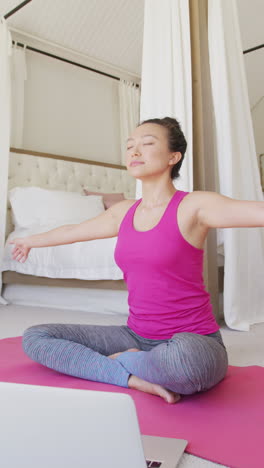 vertical video of happy asian woman doing yoga and meditating in bedroom, in slow motion