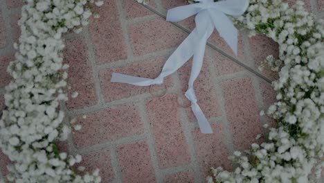 two wedding rings tied with white ribbon on a baby's breath wreath over brick pavement