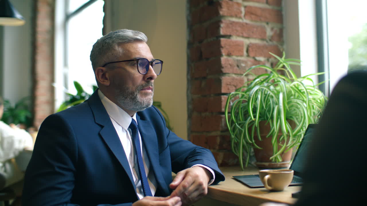 Mid-Aged Businessman Explaining Ideas to Colleague over Coffee at Cafe