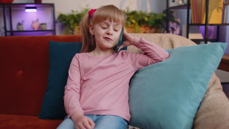 Girl-kid-enjoying-conversation-on-mobile-phone-with-friend-relaxing-sitting-on-couch-at-home-alone