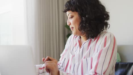 Happy-biracial-woman-in-wheelchair-talking-on-phone-using-laptop,-with-male-partner-in-living-room