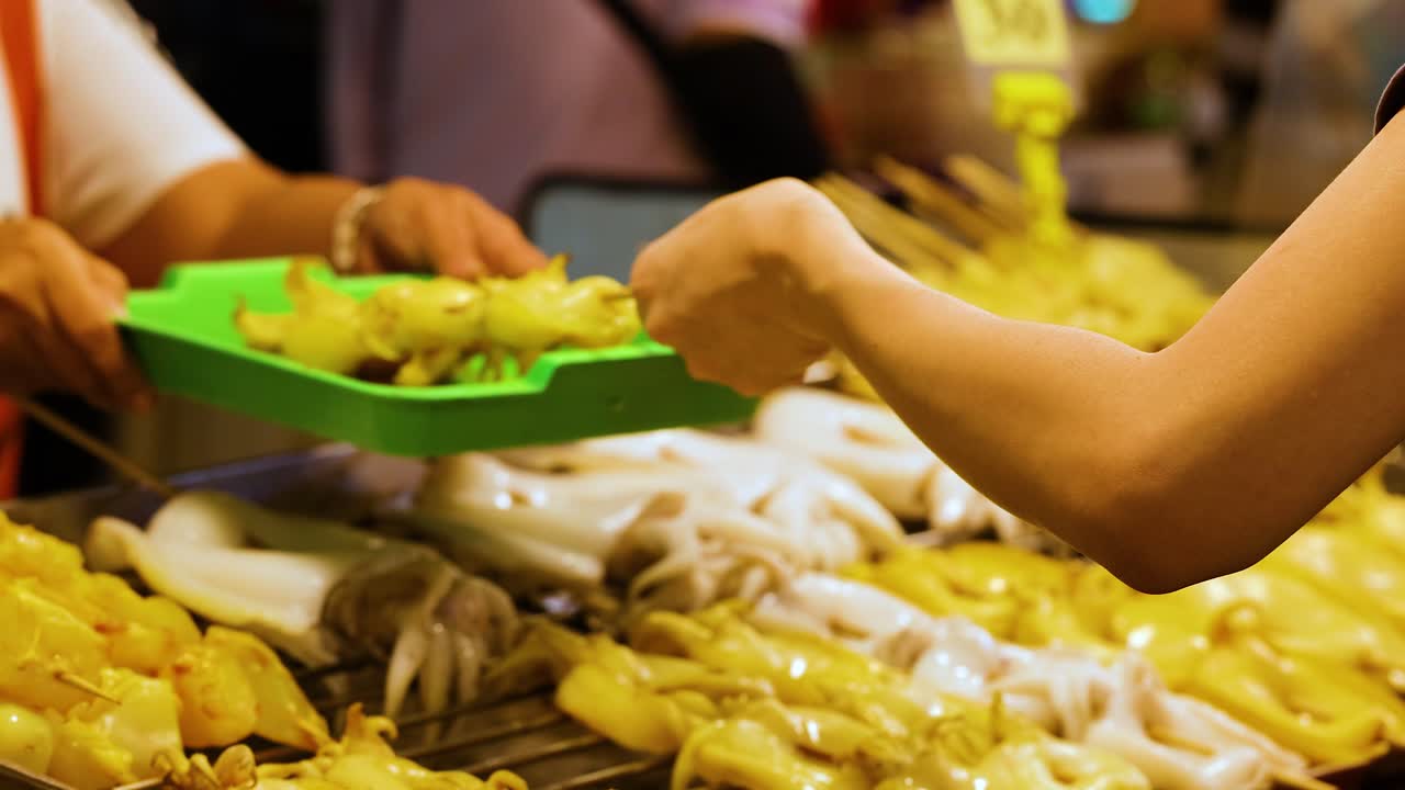 manos seleccionando pinzas de calamar a la parrilla en el mercado