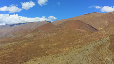 AERIAL---dry-hills-under-a-beautiful-blue-sky-and-white-puffy-clouds,-circle-pan