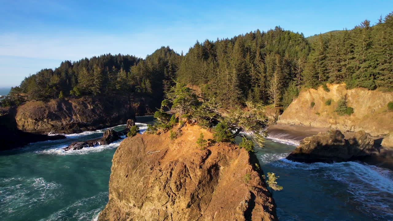 A drone rotating around a large sea stack with the ocean, cliffs and a secluded beach around.