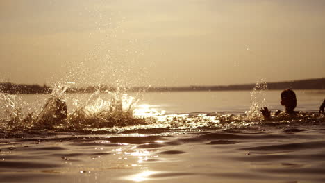 happy boys are jumping and making splashes in water at sunset. silhouette of two cheerful brothers having fun in water in the evening. summer fun.