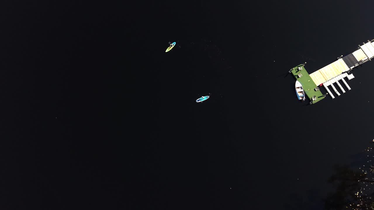 Top-down aerial view of two paddleboarders floating on dark calm Gulf of Mexico water bay near boat dock, 30A, Florida, USA