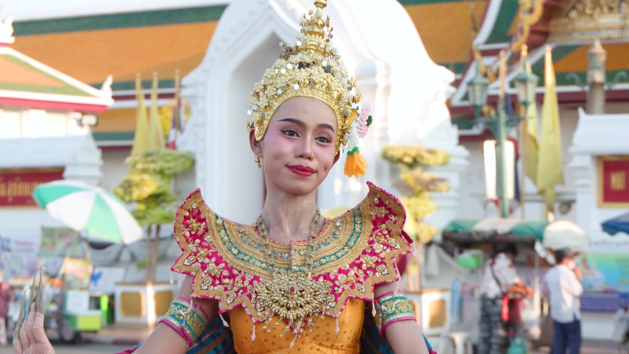 Uma dançarina em traje tradicional ornamentado realiza movimentos graciosos em frente a um templo histórico.