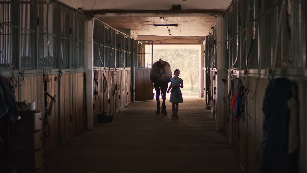 Girl Walking a Horse Through a Stable Corridor