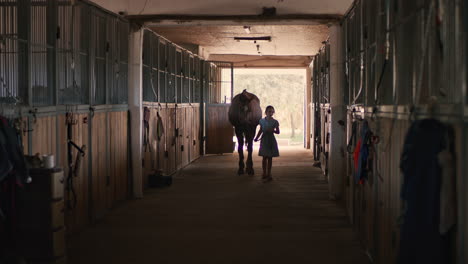 girl walking a horse through a stable corridor