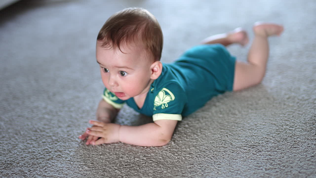 Little child banging his hands over the floor happily. Beautiful kid lies on a carpet looking up with interest.