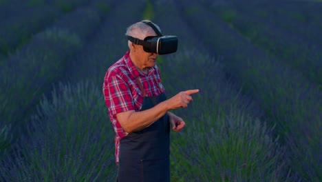 Senior-old-grandfather-farmer-in-virtual-reality-helmet-in-field-of-lavender-flowers-for-management