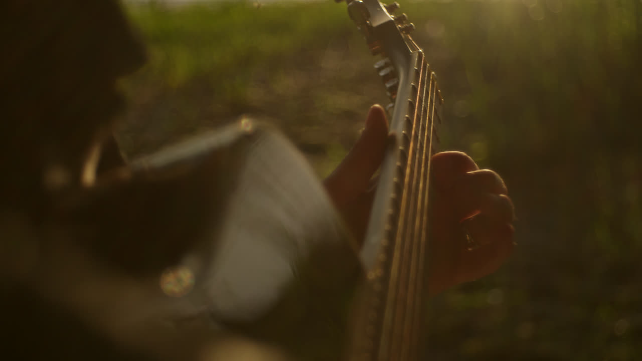 Person playing guitar outdoors in sunlight